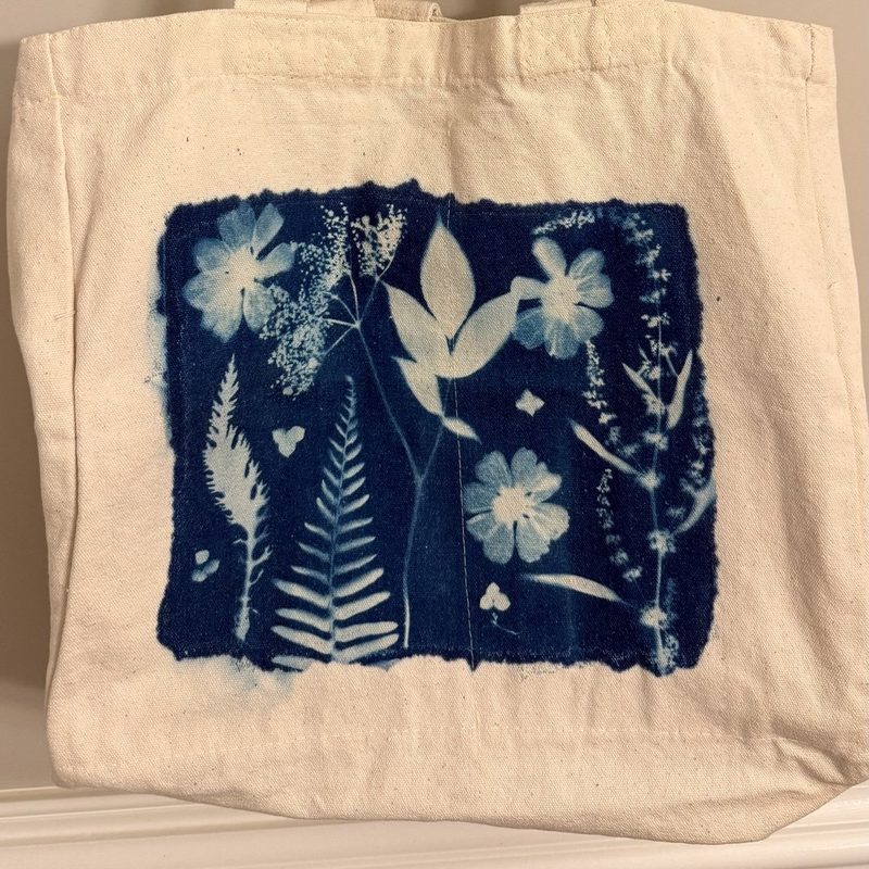 Bonus 1: a finished canvas tote bag with a deep blue cyanotype panel of ferns and flowers, hanging on a wall hook